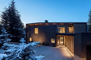 Une maison moderne dotée d’un toit incurvé, de grandes fenêtres et d’une entrée bien éclairée.
