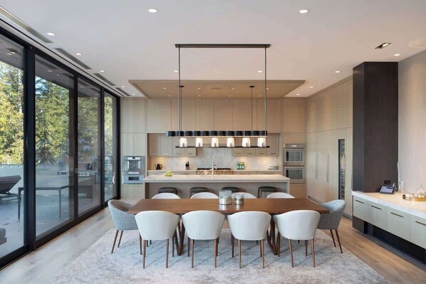Una cocina moderna con una isla central, ventanas amplias y un comedor con sillas.