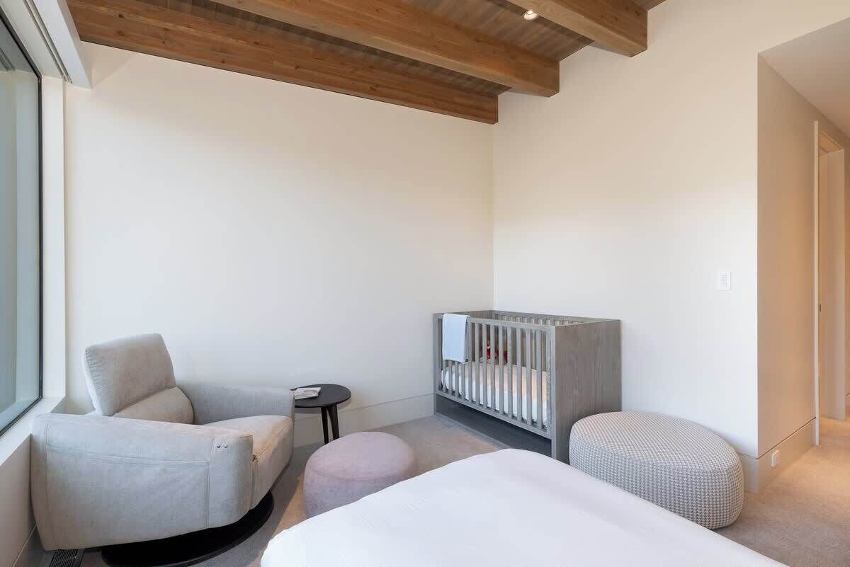 Een moderne, minimalistisch ingerichte kamer met een ledikantje, een bank, een rond voetenbankje en een kleine tafel.