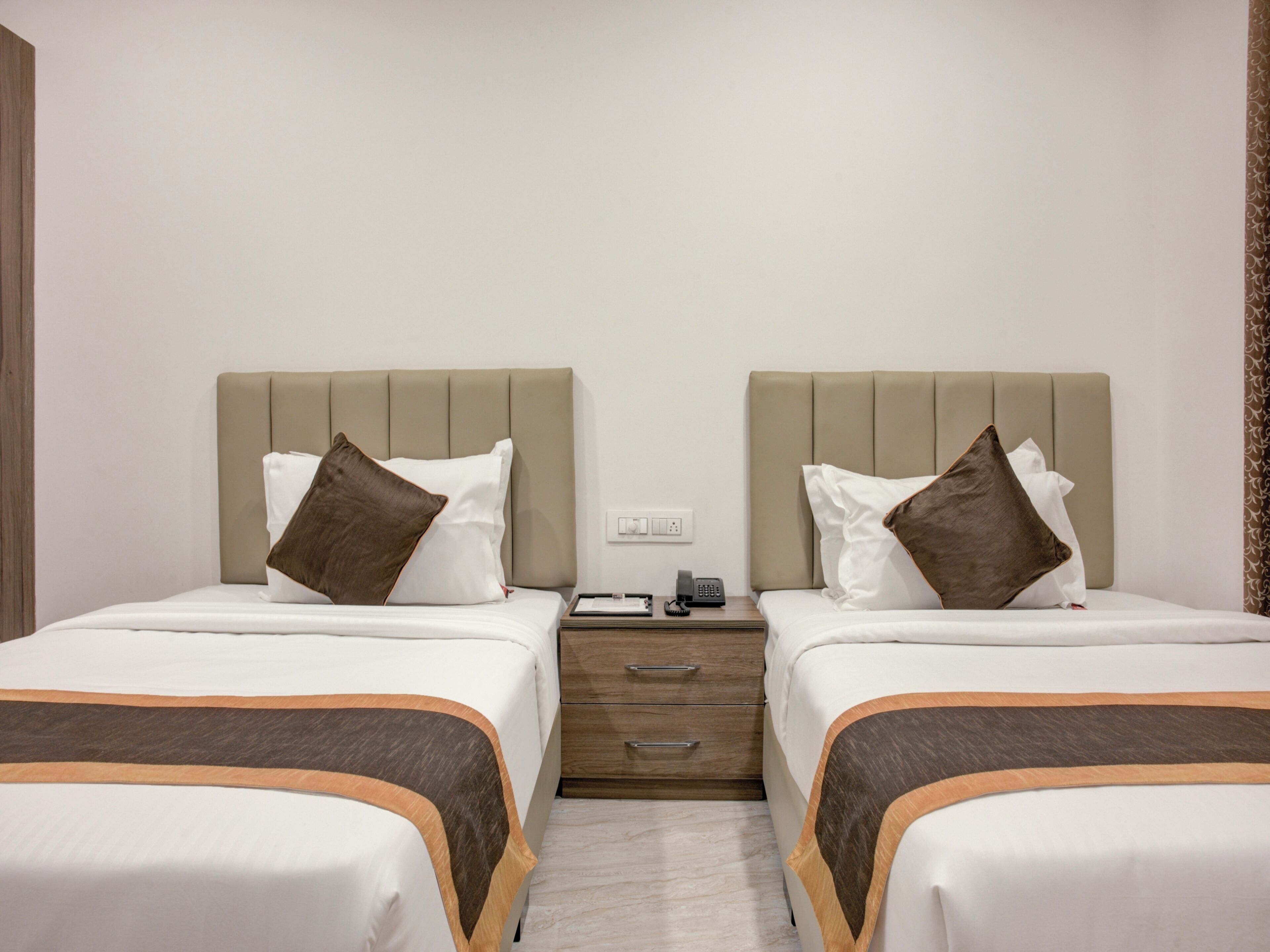 Habitación de hotel con dos camas, cada una con cabecera, mesita de noche con teléfono y cajón.