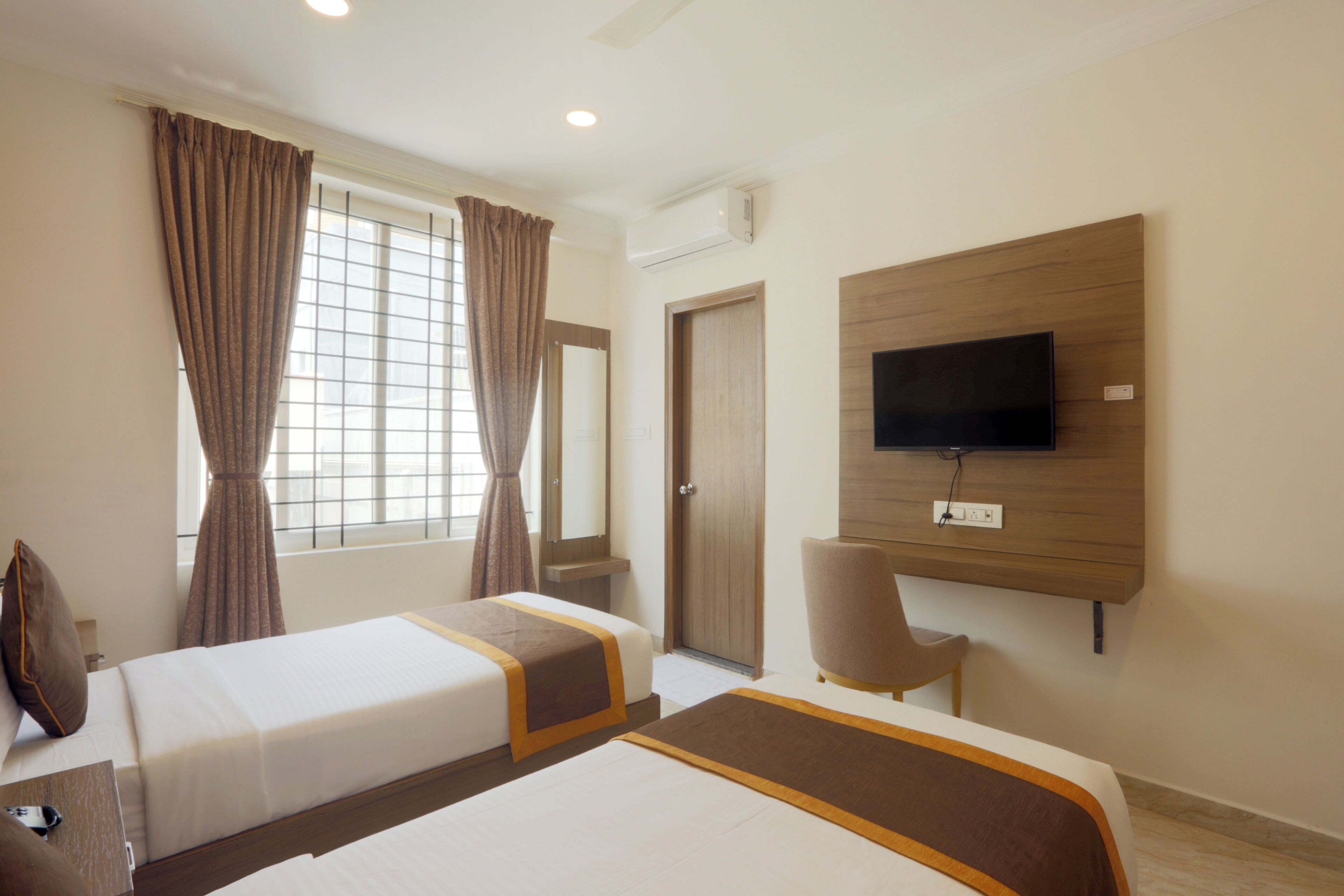 A hotel room with two beds, a TV mounted on the wall, a window with curtains, and a door.