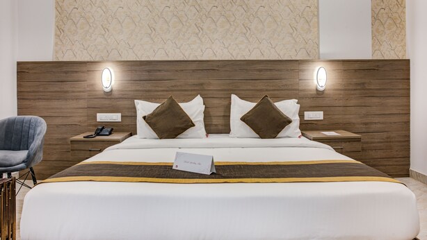 Habitación de hotel con una cama grande, dos mesitas de noche, una silla y una pared con un diseño texturizado.