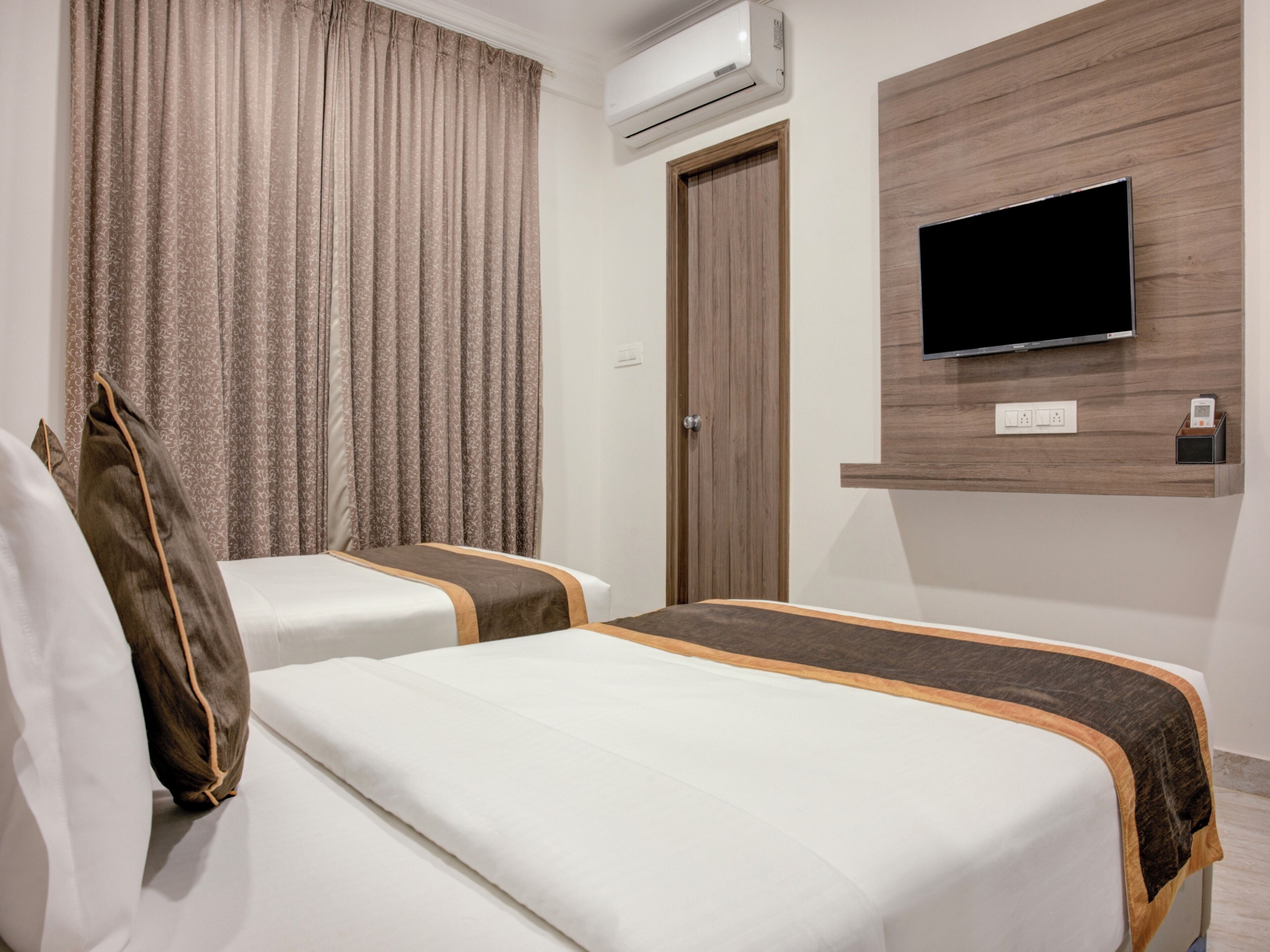 A hotel room with two beds, a TV mounted on the wall, an air conditioning unit, and a wooden panel design.