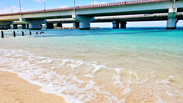 Een strand met een brug over helder turquoise water.