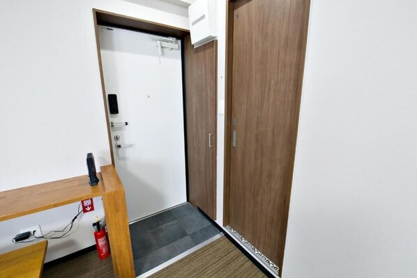 A hallway with a wooden desk, a white door, and a fire extinguisher. - TOMMY CONDOMINIUM WAKASA 301 (Naha)