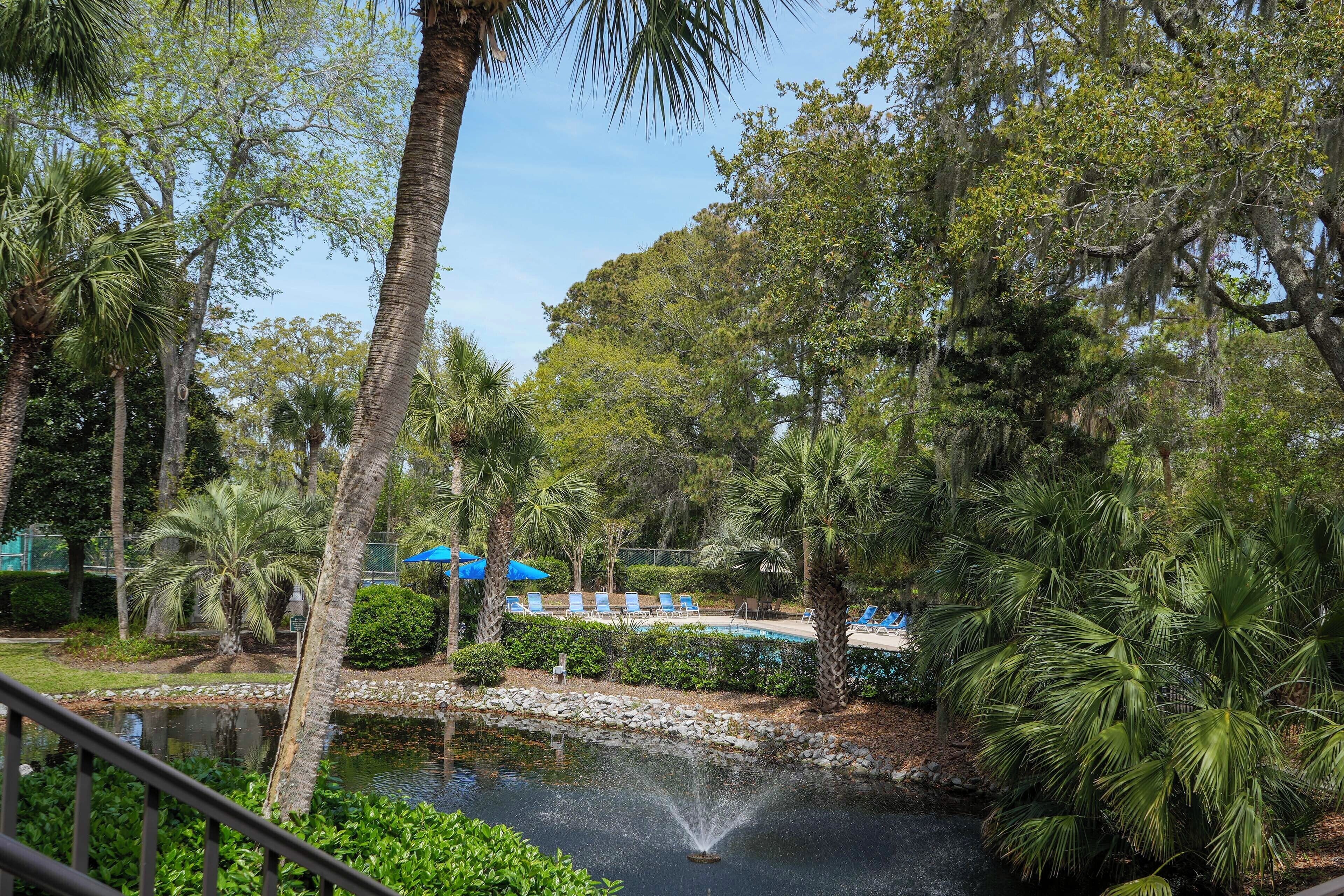 A serene outdoor area with a pond, palm trees, and a pool with lounge chairs.