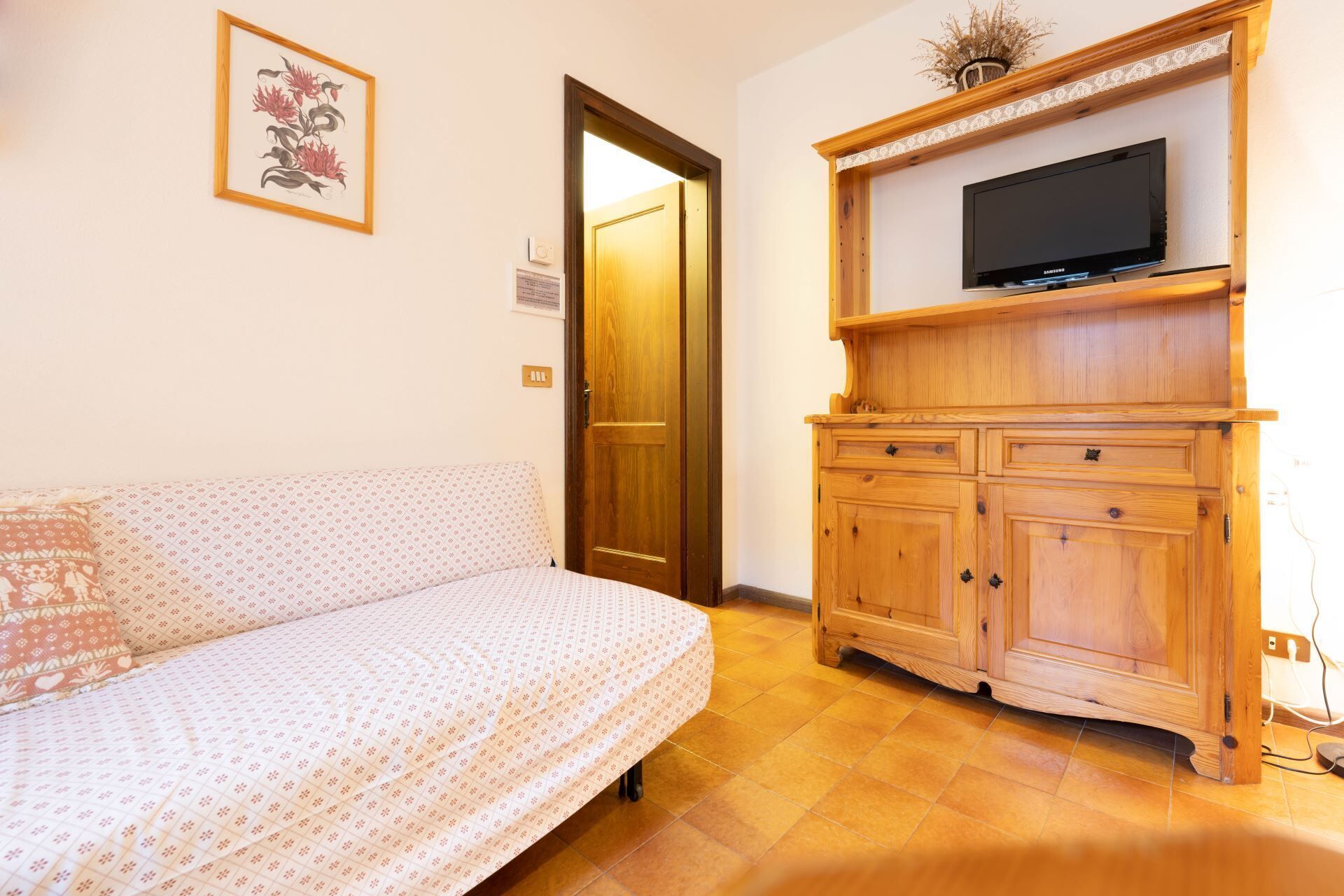 A room with a bed, wooden cabinet, and a television on a shelf.