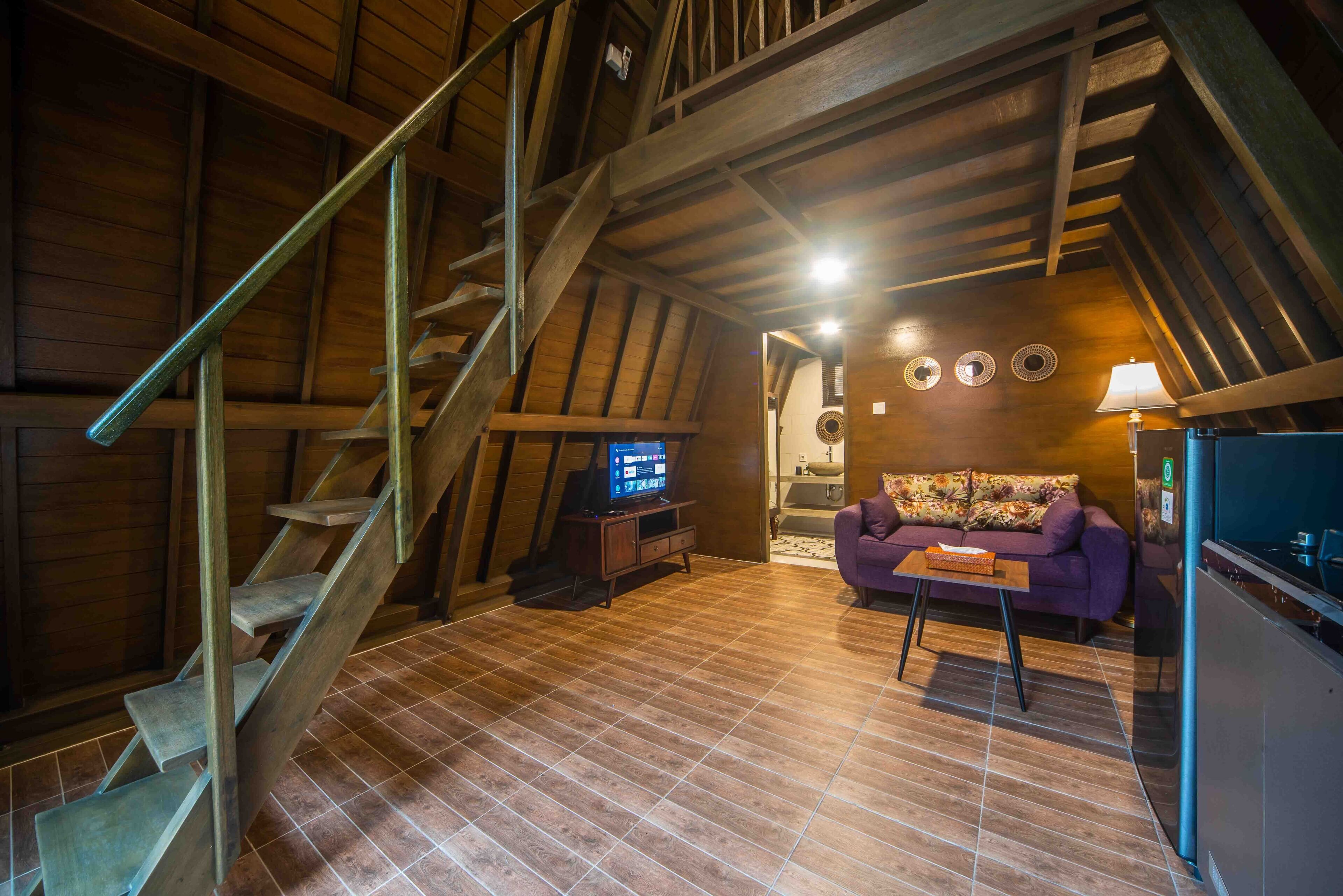 Un loft con escalera de madera, televisor, sofá púrpura y una mesita.