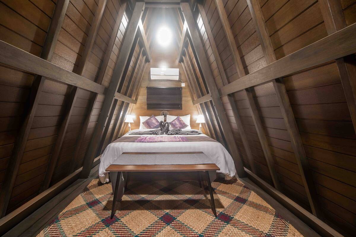 Una habitación con techos altos y vigas de madera, una cama con colcha blanca, un banco y un tapiz estampado.