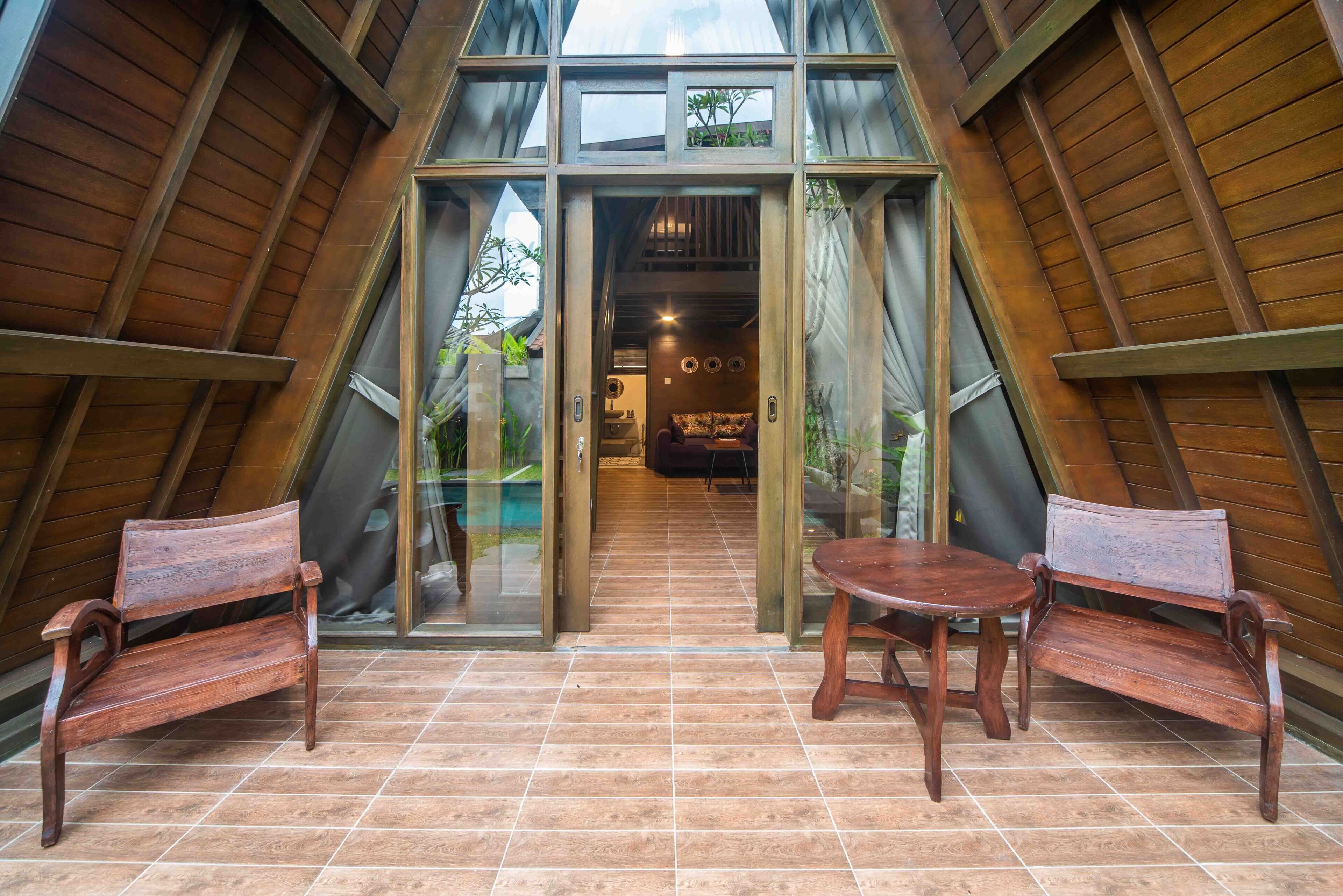 Un interior con un banco y una mesa de madera, un acceso por puerta de vidrio y vista al exterior.