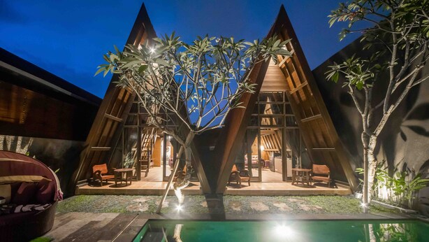 Una villa moderna con piscina, zona de estar exterior y un árbol en el centro.