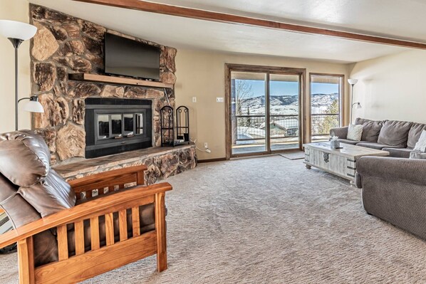 A living room with a stone fireplace, a sofa, a bench, and a view through glass doors.
