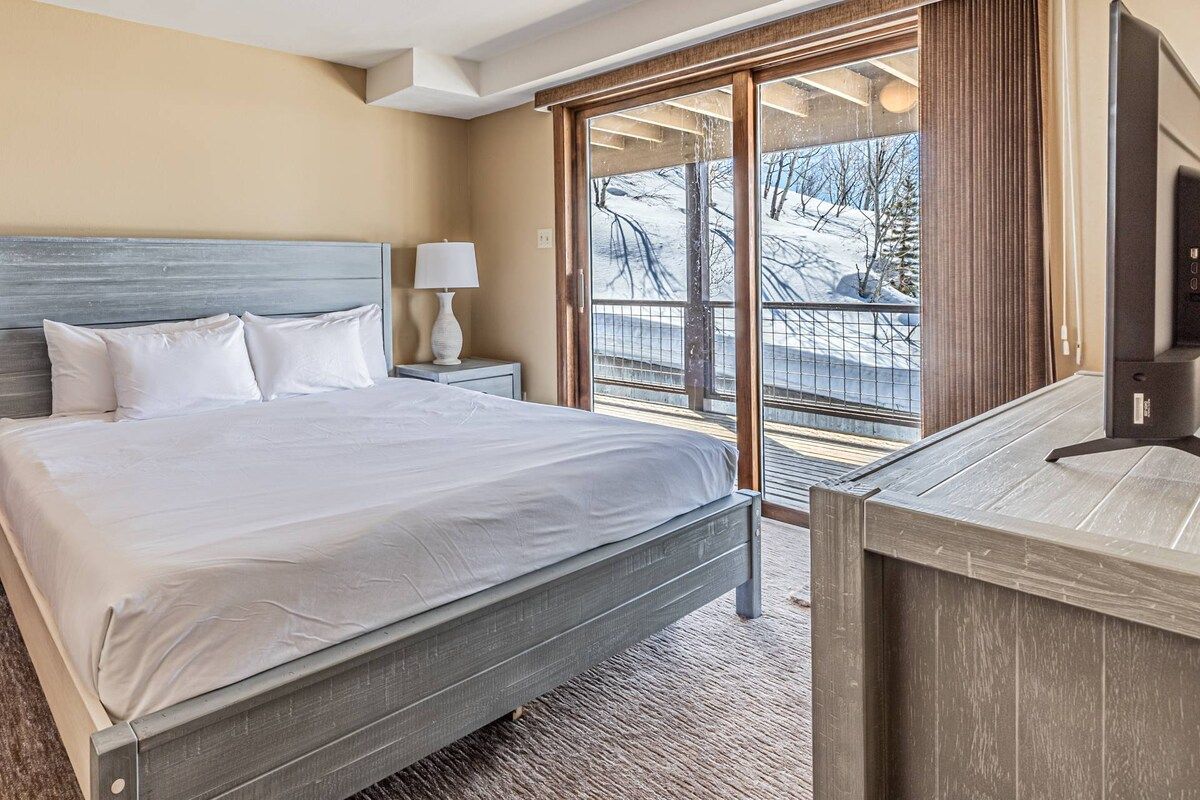 Une chambre d’hôtel avec un grand lit, une télévision, une lampe et une vue sur un paysage enneigé, visible à travers une porte coulissante.