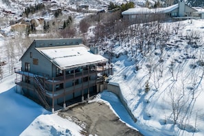 A large, multi-story building with a snow-covered roof, situated on a snowy hillside with a view of surrounding houses.