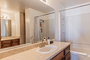 A bathroom with a sink, mirror, shower, and towel rack.