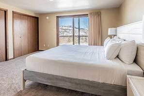 A bedroom with a large bed, a window with a view of a snowy landscape, and a wooden door.