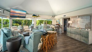 A spacious living room with a large TV, comfortable seating, a dining area, and a view of lush greenery outside. - Poseidon's Paradise: Luxury Waterfront Rental in Key West, Stunning Backyard Oasis and Private Pool! (Key West)