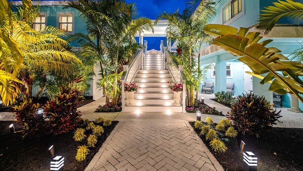A well-lit pathway leading to a building with a staircase, surrounded by tropical plants and a clear night sky. - Poseidon's Paradise: Luxury Waterfront Rental in Key West, Stunning Backyard Oasis and Private Pool! (Key West)