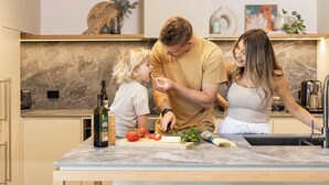 Una cocina moderna con encimera de mármol, tabla de cortar con verduras y una botella de aceite de oliva.