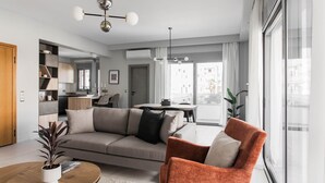 Una sala moderna con un sofá, un sillón y una mesa de centro. Se ve una cocina al fondo con una zona de comedor.