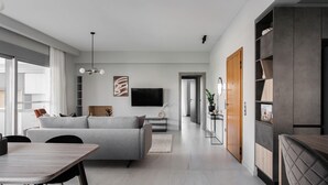 Un salón moderno con un sofá gris, una mesa de comedor y un televisor instalado en la pared.