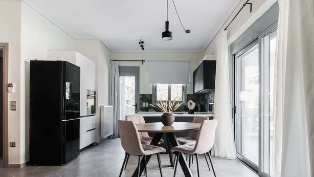 Una cocina moderna con comedor, que incluye una mesa redonda con sillas, un refrigerador negro y un amplio ventanal con cortinas.