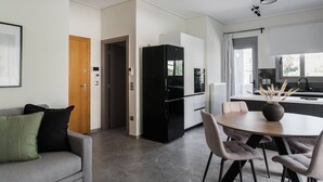 Una cocina moderna con un refrigerador negro, un comedor con una mesa redonda y sillas, y una puerta de madera que da a otra habitación.