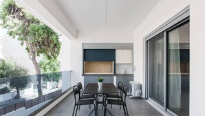 Un balcón con una mesa y sillas de comedor, una planta en maceta y vistas a árboles y una cerca.