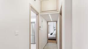 A narrow hallway leading to a bedroom with a bed, a bedside table, and a mirror.