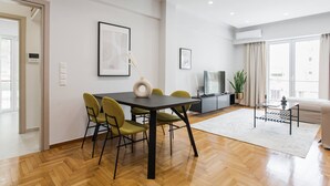A modern living room with a dining area, featuring a sofa, TV, and a dining table with chairs.