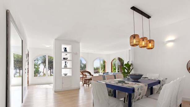 Ruime eethoek met een grote tafel, witte stoelen en een hangende lamp.