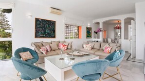 Een moderne woonkamer met een beige modulaire bank, twee blauwe fauteuils, een glazen salontafel en decoratieve kussens.