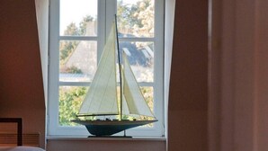 Een kamer met een raam, een bed en een klein modelzeilboot.