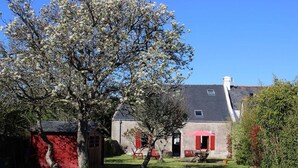 Een klassiek huis met een rode gevel, een grijs dak en een tuin met een bloeiende boom.