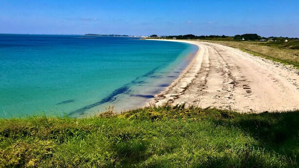 Een strand met helder turquoise water en een zandpad dat naar het strand leidt.