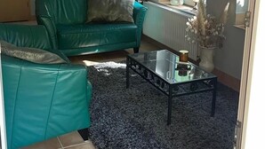 Een woonkamer met een groene bank, een glazen salontafel en een blauw vloerkleed.