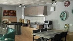 Een keuken met een eethoek, met een betegelde vloer, een eettafel met stoelen, een magnetron en een spoelbak.