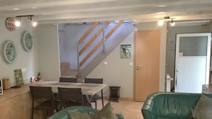 Een eethoek met een tafel en stoelen, een trap, een groene bank en een deur met ruitverdeling.