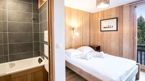 Een slaapkamer met een houten bed, een wit wandlampje en een afbeelding in een lijst.