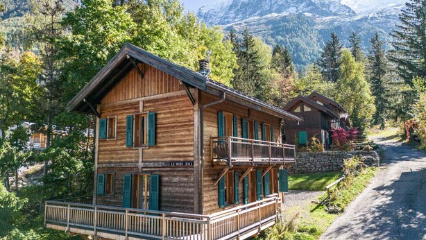 Een houten chalet met balkon, omringd door bomen en bergen.