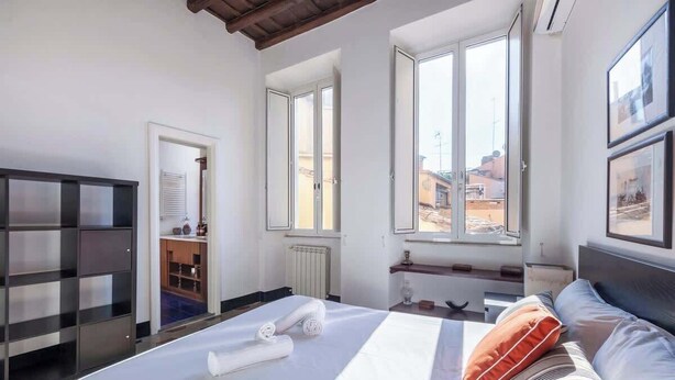 Una habitación de hotel con cama, armario, ventana con vistas y una pequeña mesa con lámpara.
