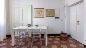 Un comedor con una mesa y sillas blancas, dos cuadros en la pared y un suelo estampado.