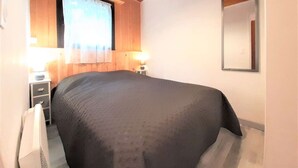 Een slaapkamer met een groot bed, houten plafond, een raam met gordijnen, een bedlamp en een spiegel aan de muur.