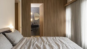 Una camera da letto con un letto, un comodino, uno specchio e un bagno visibile attraverso una porta.