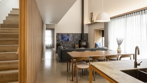 Une cuisine moderne avec un coin repas, un escalier en bois et un salon doté d’un canapé et d’une télévision.