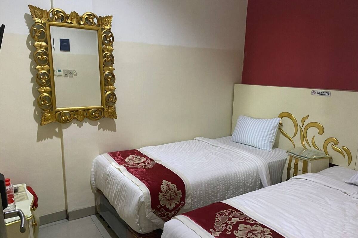 Habitación de hotel con dos camas, un espejo con marco dorado y una pared de acento roja.