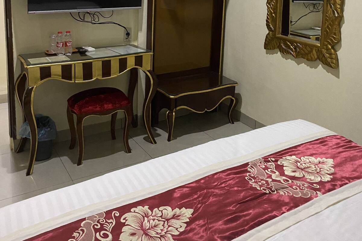 Una habitación de hotel con una cama, un escritorio con televisor, un espejo y una silla.