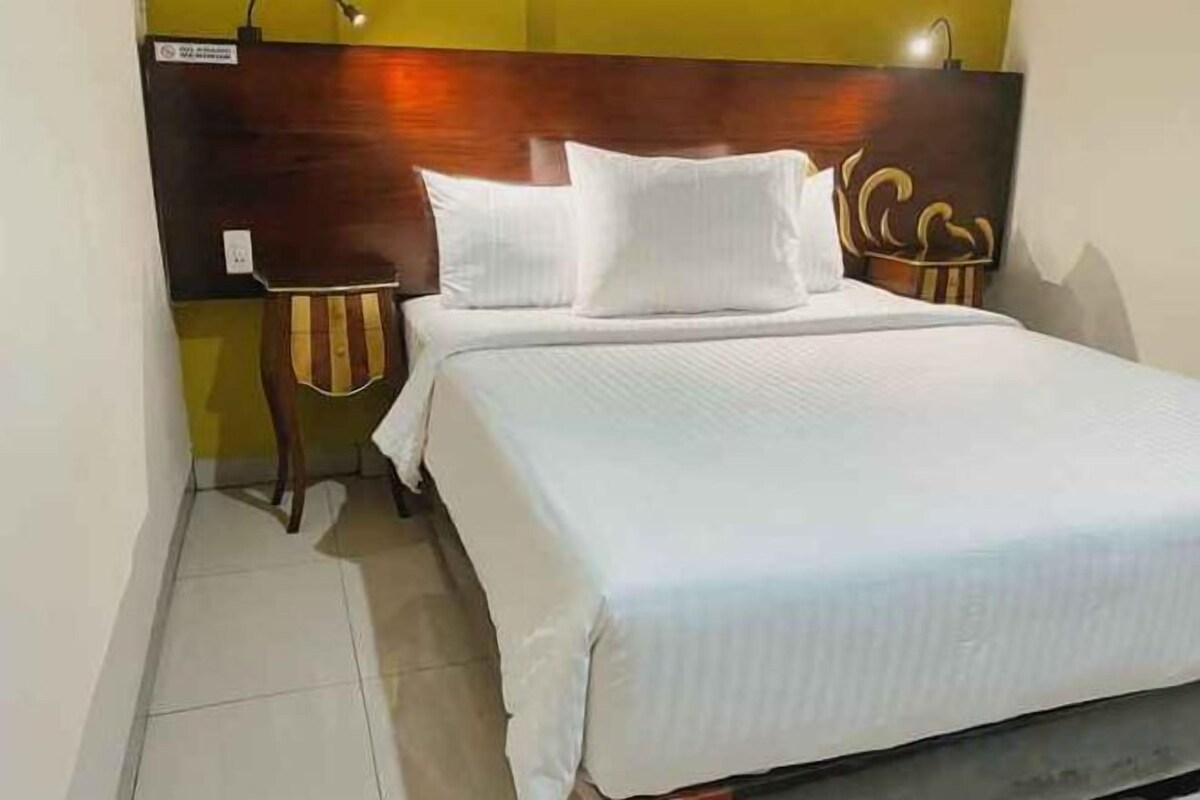 A neatly made bed with white linens in a room with a wooden headboard and a small side table.