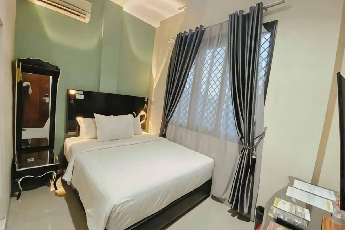 Una habitación de hotel con cama, espejo, mesita de noche y ventana con cortinas.