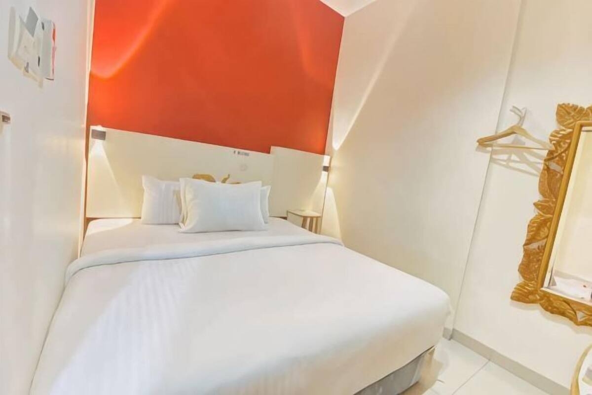 Una habitación de hotel con cama, lámparas de noche, un espejo y perchero en la pared.
